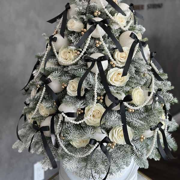Snow-dusted evergreen tree with white roses, black ribbons, and pearl garlands