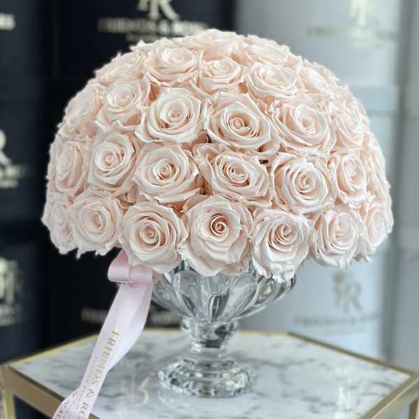 A dome of pale pink roses in a clear glass vase with a pink ribbon.