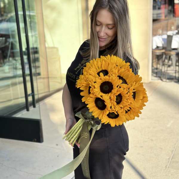 Woman holding a bouquet of bright yellow sunflowers with a ribbon wrap