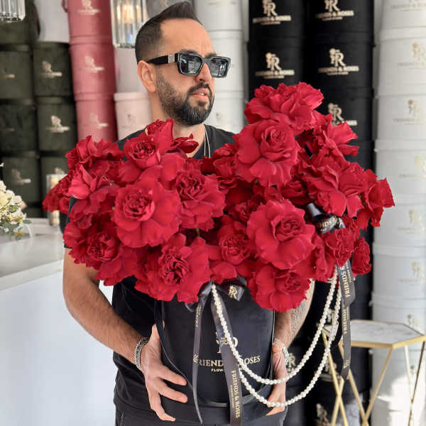 Man holding a large box of red roses with ribbon and pearl strands