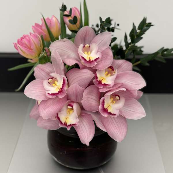 Pink orchids and tulips arranged in a dark glass vase