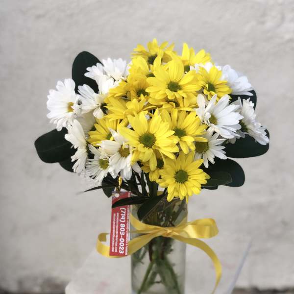 Bouquet of yellow and white daisies in a glass vase with a yellow ribbon