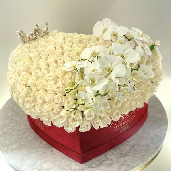 Heart-shaped box of cream roses with white orchids and a small crown