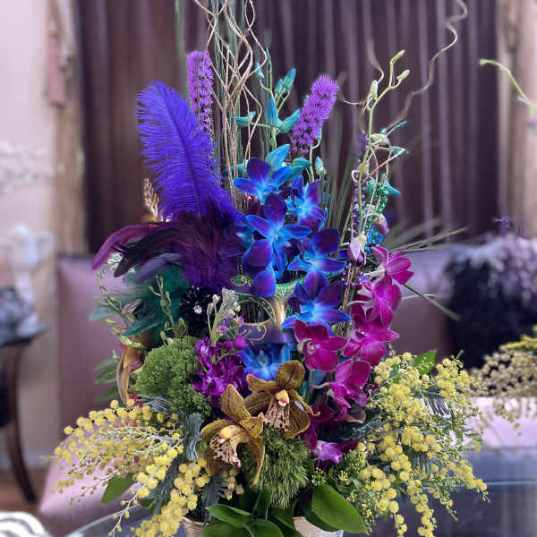 Tall colorful floral arrangement in a gold vase with orchids and feathers