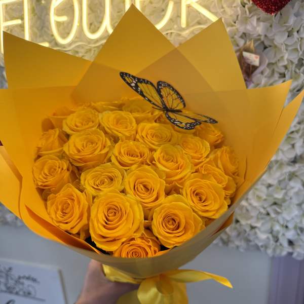 Bouquet of yellow roses wrapped in bright yellow paper with a butterfly decoration
