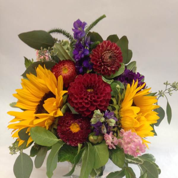 Mixed bouquet with sunflowers, purple blooms, and red dahlias in a glass vase