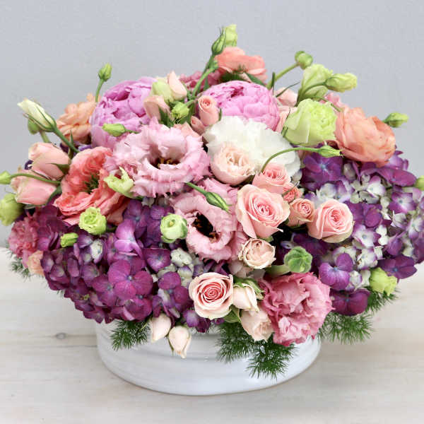 Low arrangement of pink and purple flowers in a white ceramic bowl