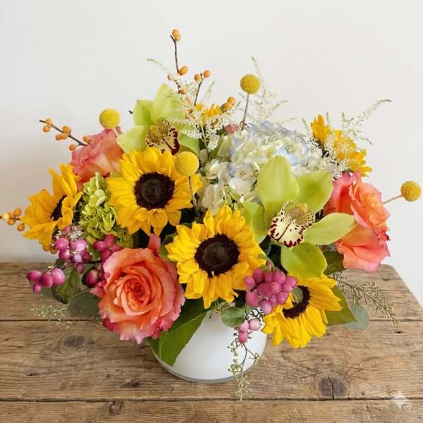 Mixed bouquet in a white vase with sunflowers, roses, and orchids