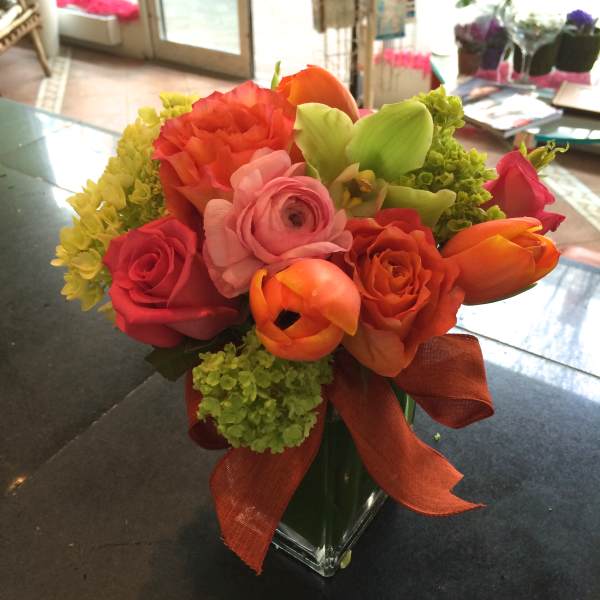 Colorful bouquet of roses and tulips in a glass vase with an orange ribbon
