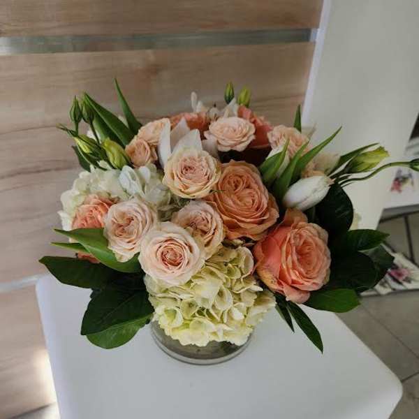 Low arrangement of peach roses and white hydrangeas in a clear glass vase on a white pedestal