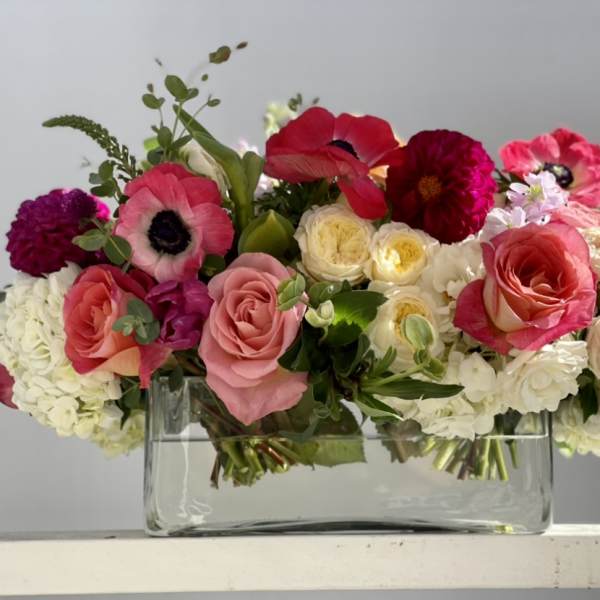 Low rectangular arrangement of pink, red, and white flowers in a clear glass vase