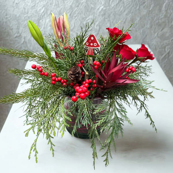 Holiday floral arrangement with red roses, lilies, and evergreen branches in a glass vase