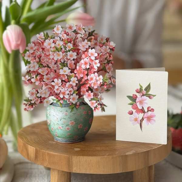 Pink cherry blossom arrangement in a green patterned vase beside a matching card
