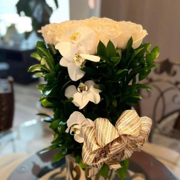 White roses and orchids in a tall arrangement with a striped ribbon bow.