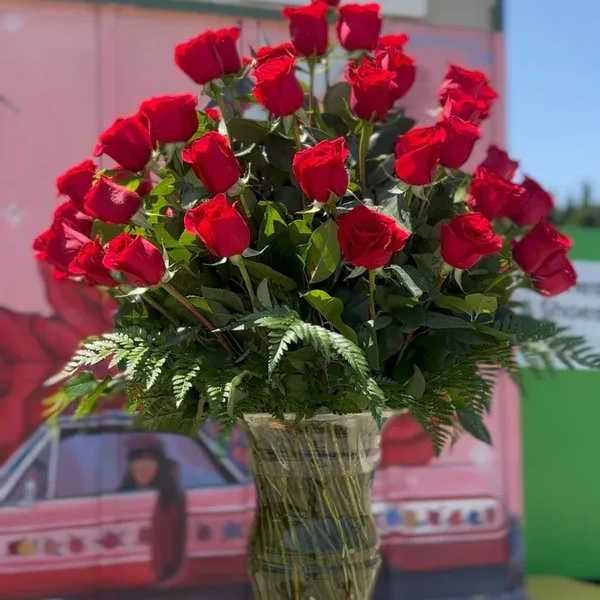 Tall vase arrangement of red roses with fern foliage
