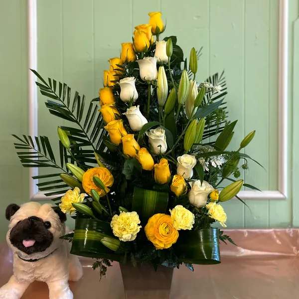 Yellow and white rose arrangement in a square vase with a plush pug beside it