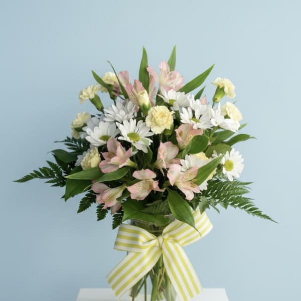 Bouquet of white daisies and pink alstroemeria in a glass vase with a striped ribbon