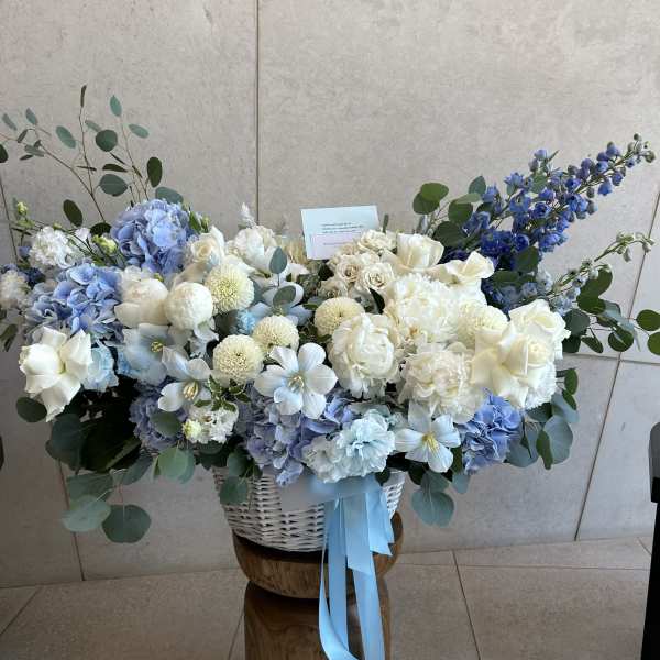 Large blue and white floral arrangement in a white basket with ribbon