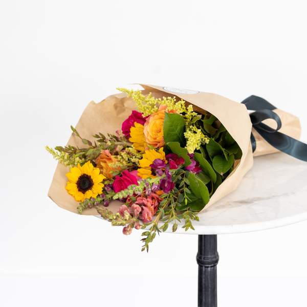 Bouquet of sunflowers, roses, and mixed blooms wrapped in tan paper
