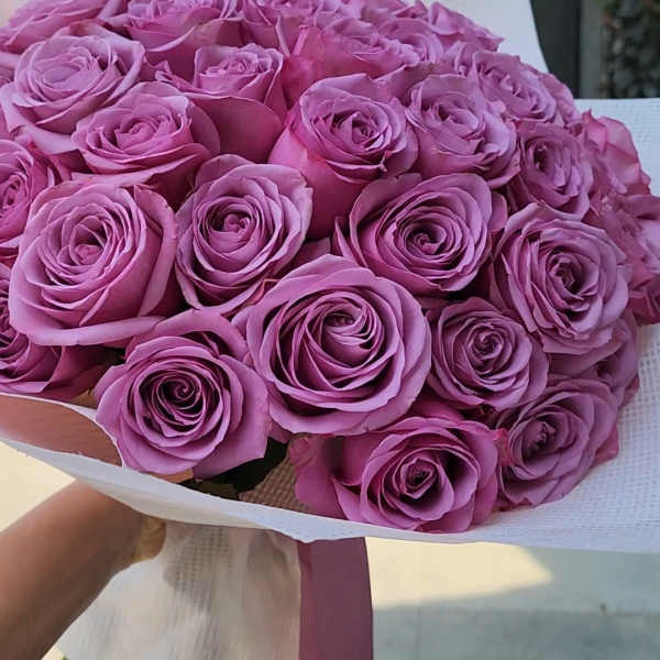Bouquet of lavender roses wrapped in white paper with a pink ribbon