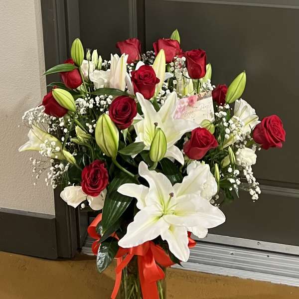 Bouquet of red roses and white lilies in a glass vase with a red ribbon