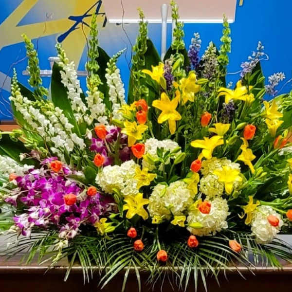 Large mixed arrangement of yellow lilies, white hydrangeas, orange tulips, and purple orchids on a table
