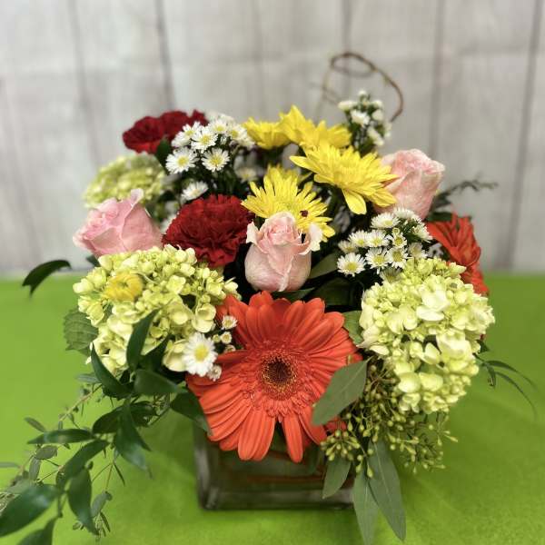 Mixed bouquet in a square glass vase with gerbera daisies, roses, and hydrangeas