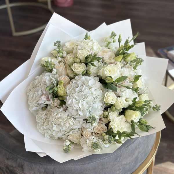 Bouquet of white hydrangeas and cream roses wrapped in white paper
