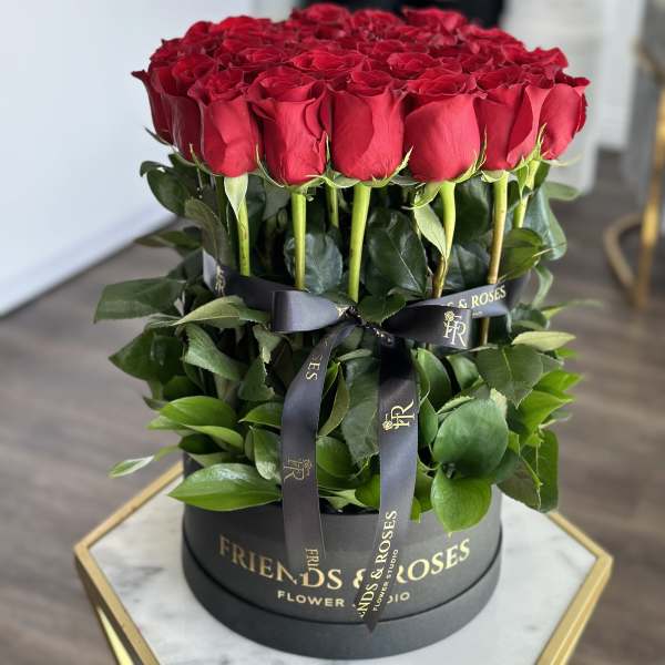 Round box of red roses with dark ribbon and greenery
