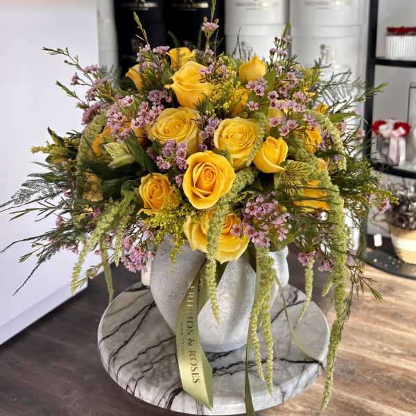 Yellow roses and pink filler flowers in a white vase