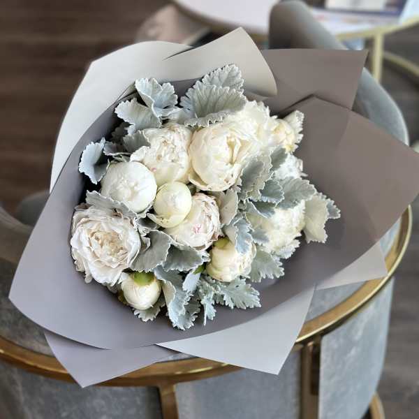 Bouquet of white peonies with silvery foliage in gray paper