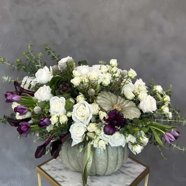 White roses and purple tulips arranged in a pumpkin vase