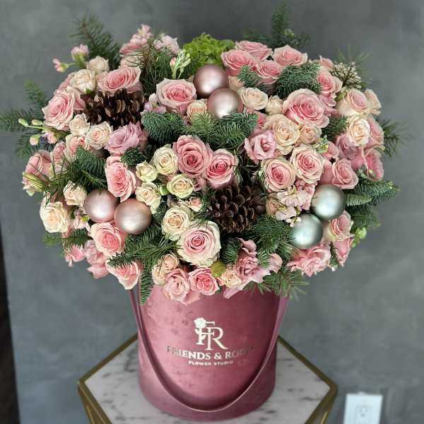 Pink and cream roses arranged in a round box with pinecones and ornaments