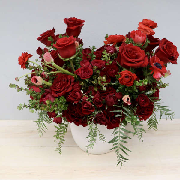 Lush arrangement of deep red roses and mixed red blooms in a white round vase