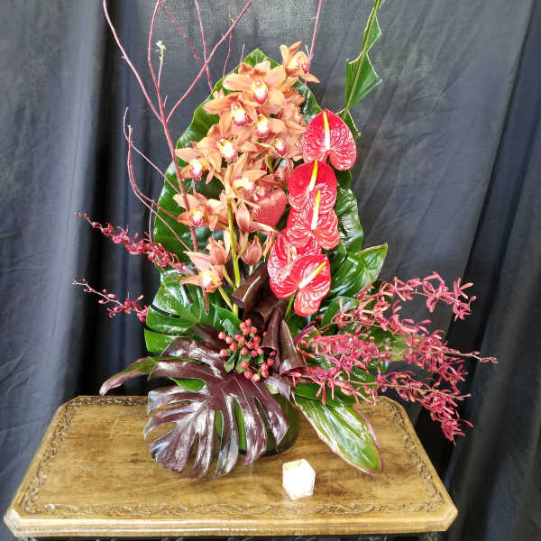 Tall tropical arrangement with orchids and red anthuriums in a vase