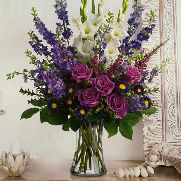 Purple roses and white gladiolus in a clear glass vase