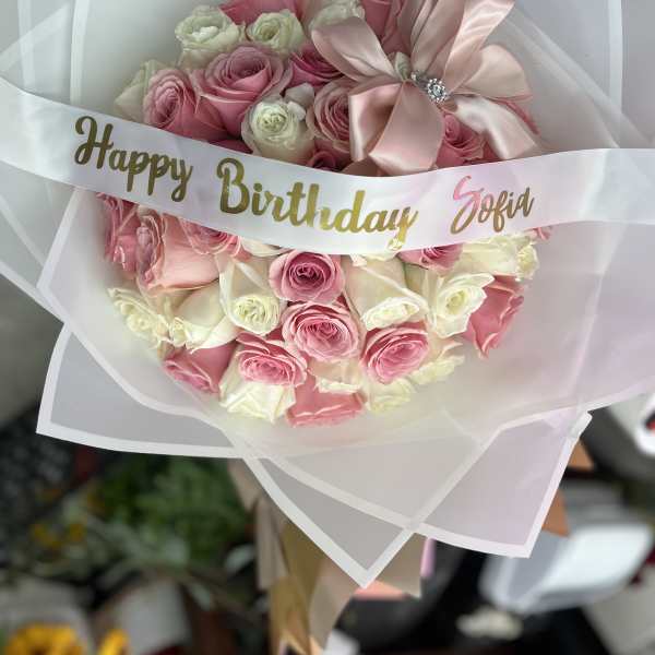 Pink and white rose bouquet wrapped in translucent paper with a birthday ribbon