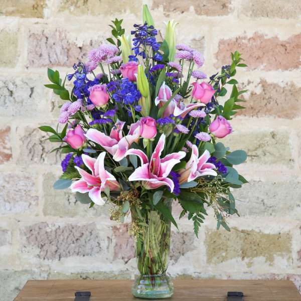 Bouquet of pink lilies, roses, and purple flowers in a glass vase