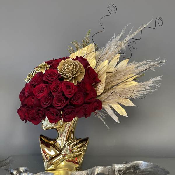 Red rose arrangement in a gold sculptural vase with dried pampas grass