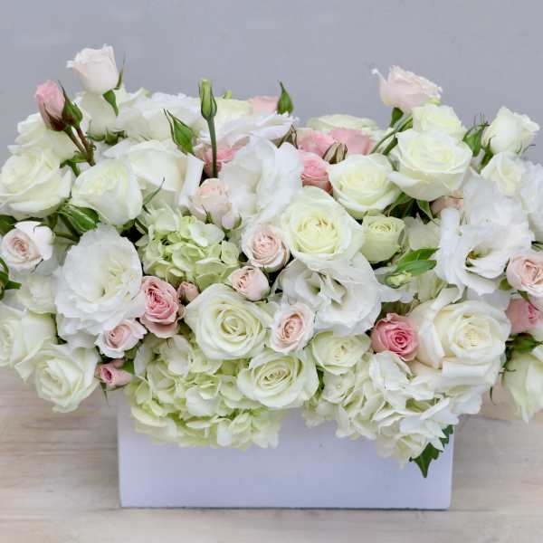 Low rectangular arrangement of white and pale pink roses and lisianthus in a white box.