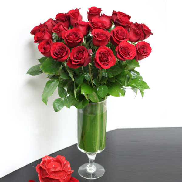 Tall glass vase filled with long-stemmed red roses and a red rose candle at the base