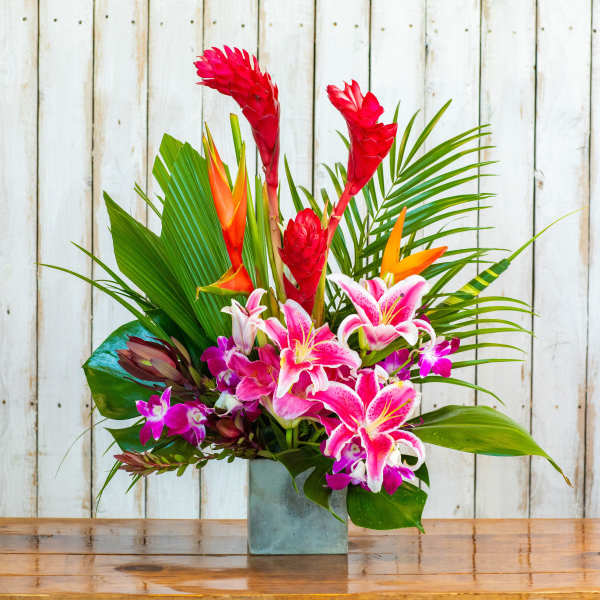 Tropical flower arrangement with pink lilies and red ginger in a square vase