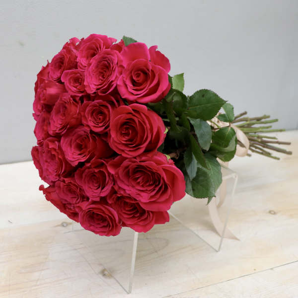 Hand-tied bouquet of hot pink roses with long stems and ribbon lying on a clear stand.