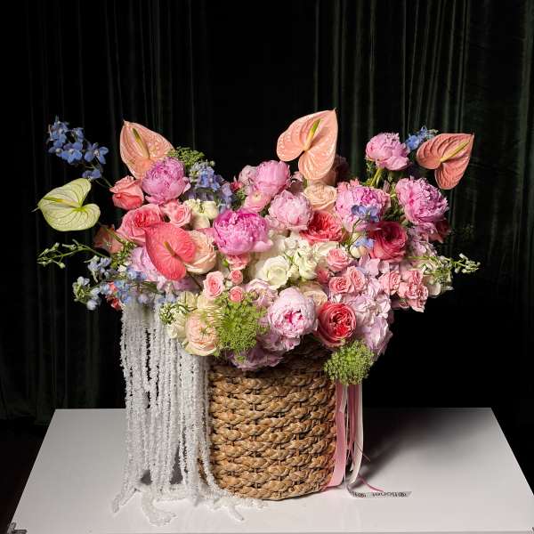 Large pastel floral arrangement in a woven basket with hanging white strands