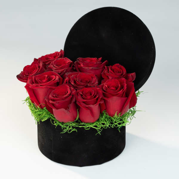 Red roses arranged in a black round box with green filler
