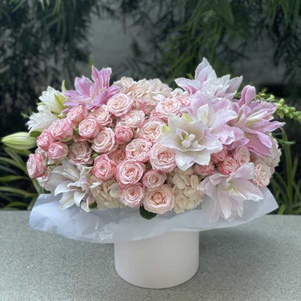 Pink roses and white lilies arranged in a white box vase
