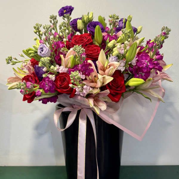 Mixed bouquet of red roses, lilies, and purple flowers in a black vase