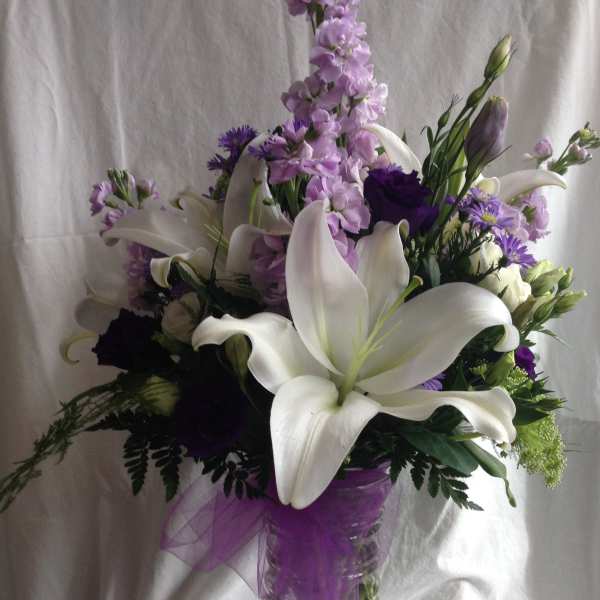 White lilies and purple flowers arranged in a glass vase with a purple ribbon.