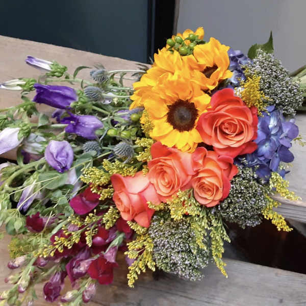 Colorful bouquet with sunflowers, roses, and purple blooms on a bench