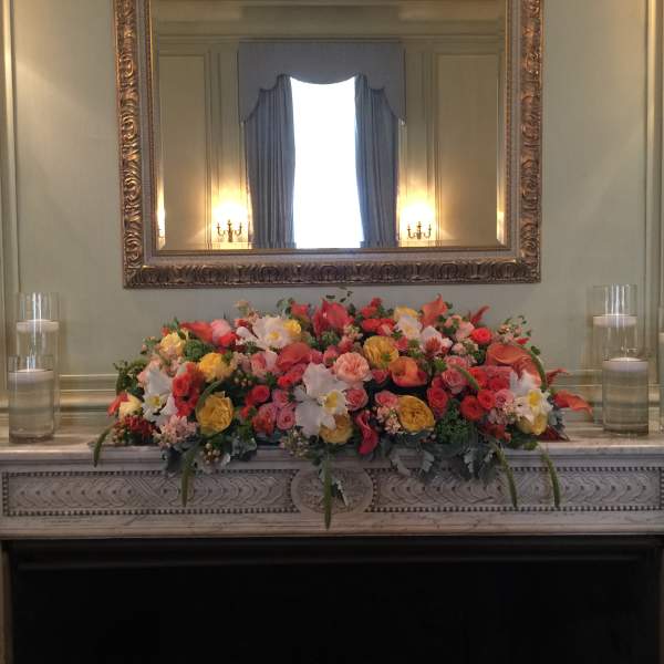 Colorful floral arrangement on a mantel with glass candles on both sides